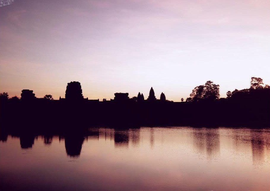 Angkor Wat silhouetted and reflected in still water under a pink-gold sky